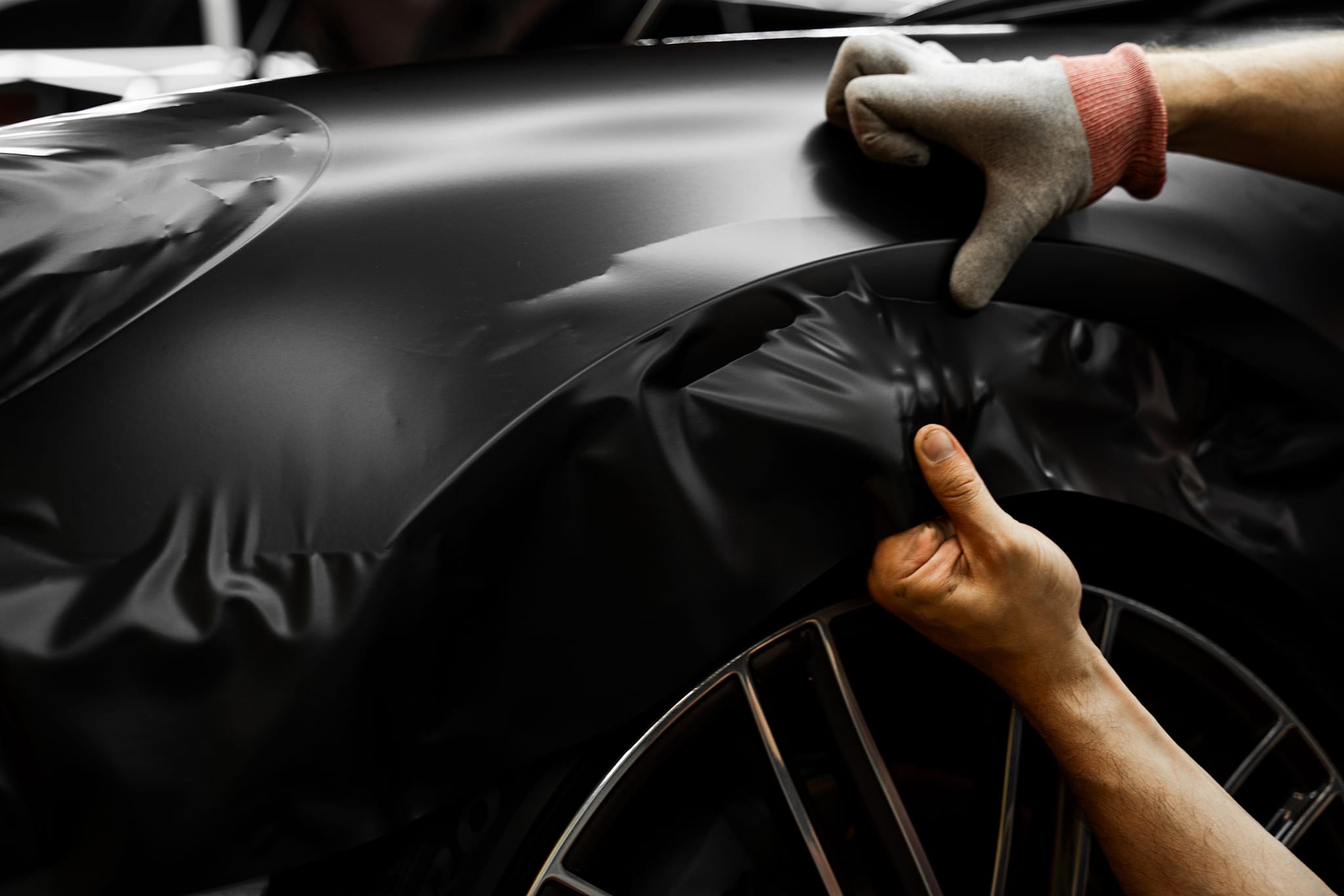 An installer stretching black film over a fender