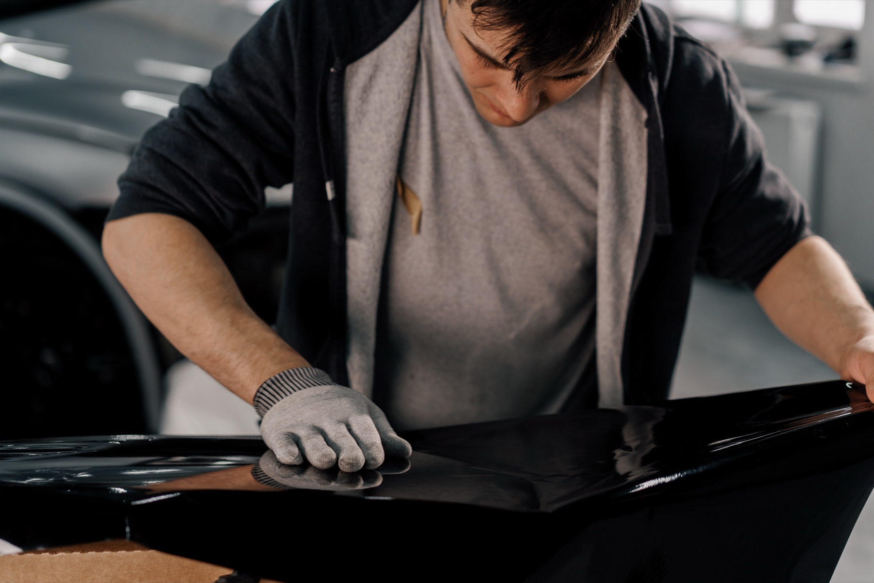 An installer laying black film on a car in the shop