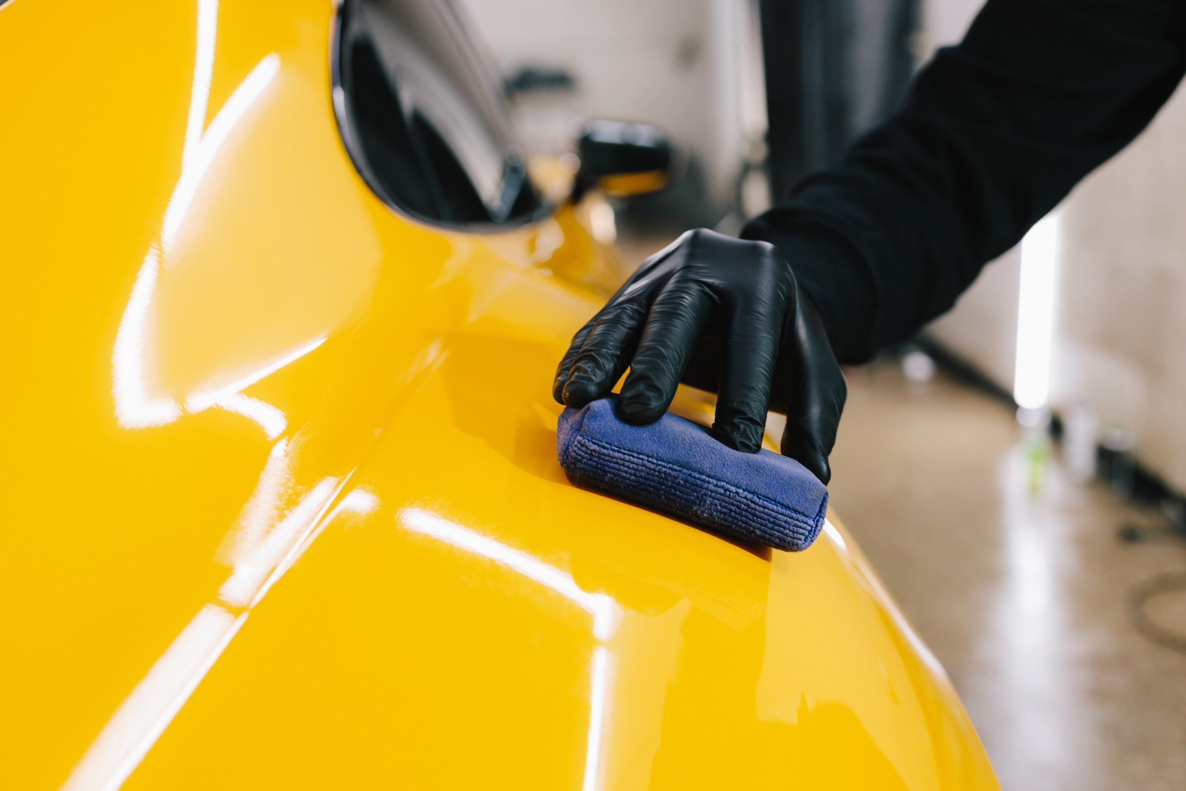 An installer in black gloves finishing the surface of a yellow car